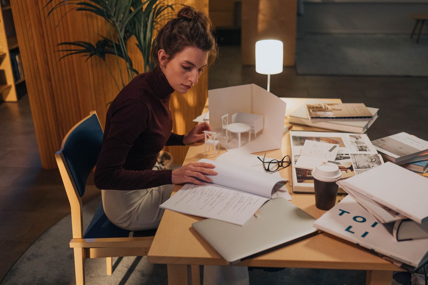 A woman working at a cluttered desk in lamplight